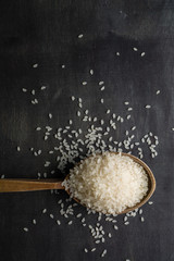 A handful of white polished rice in a wooden old spoon. Dark wood background. View from above. Space for text.