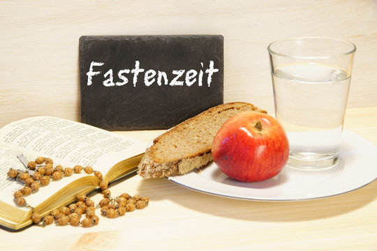 Fastenzeit, Tafel mit Schrift, Gebetbuch, Brot, Apfel, Glas Wasser