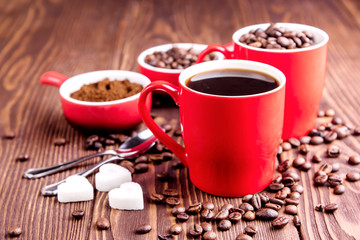 Two cups with coffee Cup with coffee beans Wooden background Coffee beans around red cups