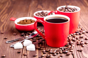 Fotobehang Two cups with coffee Cup with coffee beans Wooden background Coffee beans around red cups © katekrsk