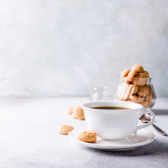 White cup of coffee with amaretti cookies on light gray background with copy space.
