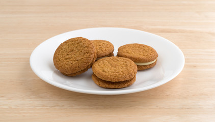 Four cheesecake filled pumpkin cookies on a white plate atop a wood table.