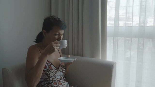 Woman drinking coffee near the window. 4K stock footage.
