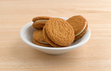 Cheesecake filled pumpkin cookies in a bowl atop a wood table.