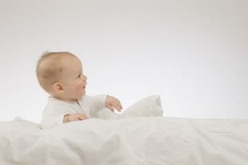 Laying funny baby boy on the white blanket. Studio shot. Isolated