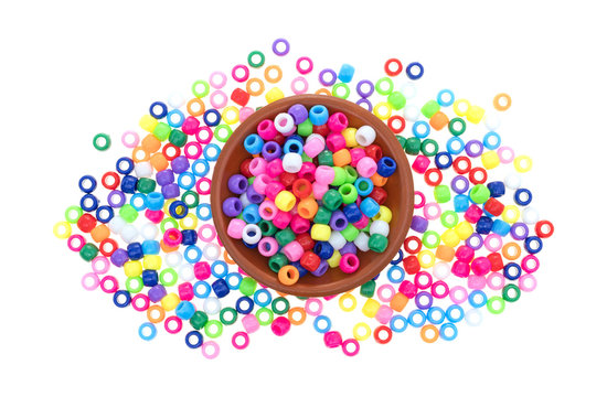Top view of a small clay bowl filled with pony beads with several beads overflowing onto a white background.