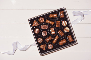 top view of various chocolate pralines in box on white wooden background.