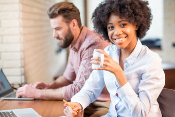 Beautiful african businesswoman and caucasian man working together with laptops and coffee cups near the window at the cafe or office