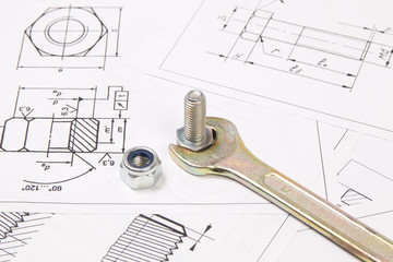 Technical drawings of bolts and nuts. Engineering, technology and metalworking. Metal bolts, nuts and wrench on printed drawings background.