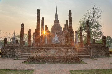 Sunset scenery of Wat Sa Si in Sukhothai Historical Park with setting sun in background and a statue of seated Buddha in the shrine of a ruined temple ~ A beautiful UNESCO heritage site in Thailand