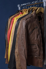 Many colored  leather jacket hanging on rack on blue background