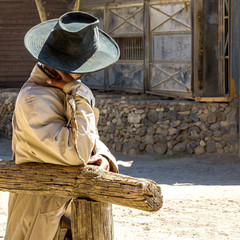 Cowboy waiting in the sun. People photo: Cowboy with hat waiting leaned against the railing in the heat of the desert
