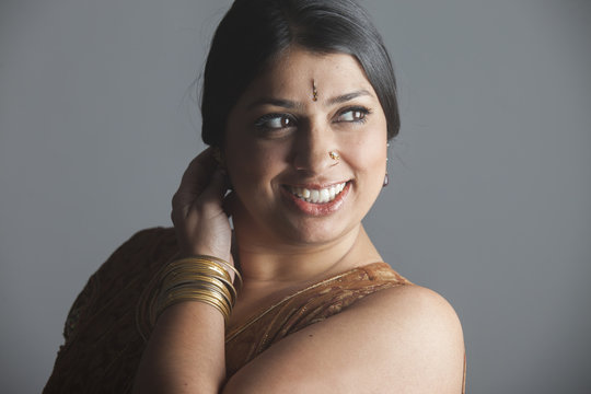 portrait of a cheerful brunette indian woman with dark skin and jewelry isolated on grey background