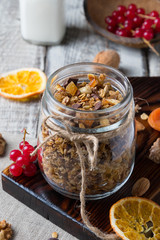 Homemade granola with nuts and dried oranges in jar and bottle of milk on wooden background