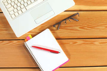 surface of a wooden table with notebook, smartphone, eye glasses, and pen