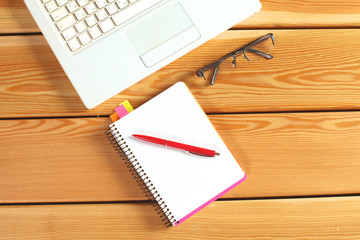 surface of a wooden table with notebook, smartphone, eye glasses, and pen