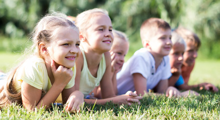 Group of positive kids lying on green grass in park