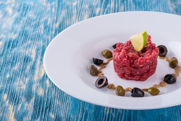 Single portion of tartar steak on white plate with capers