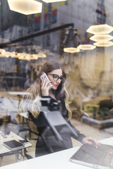 Beautiful young business woman talking on mobile phone and searching for informations at her laptop.