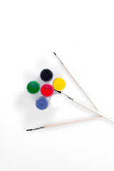 Jars with colored gouache and brush for drawing on a white background laid out in the shape of a flower.