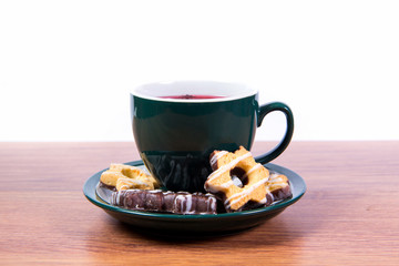 A cup of fragrant black tea in a porcelain mug and shortbread covered with chocolate on a plate - delicious breakfast for your favorite.
