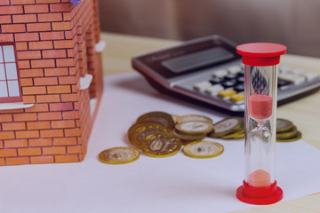 Home and money, hourglass and calculator on table close-up