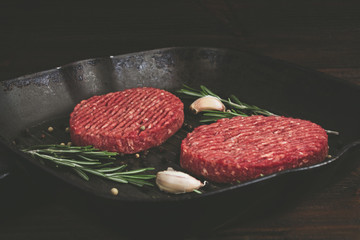 Raw cutlets pan with rosemary and garlic. Wooden brown background.