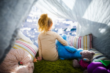 Little girl with teddy bear in camp tent looking at the sea