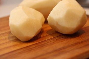 Peeled potatoes in wooden chopping board.