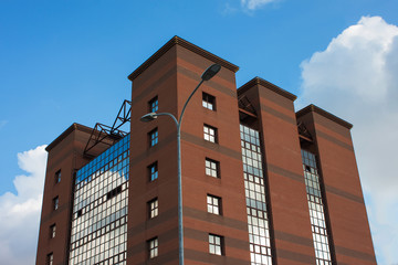 moderno edificio di mattoni e vetro su uno sfondo di cielo blu con nuvole. lampione coincide con il bordo dell'edificio. Alcune finestre sono aperte.