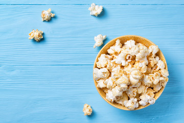 Sweet popcorn in a yellow bowl on a blue wooden background, top view