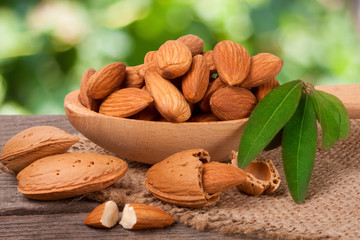 heap of peeled almonds with leaf in a wooden spoon on table blurred garden background