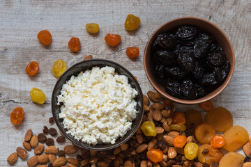 cottage cheese in white plate and the prunes in the brown plate. Prunes, dried apricots, dried mandarins and almonds on a light wooden background