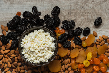 cottage cheese in white dish. Prunes, dried apricots, dried mandarins and almonds on a light wooden background