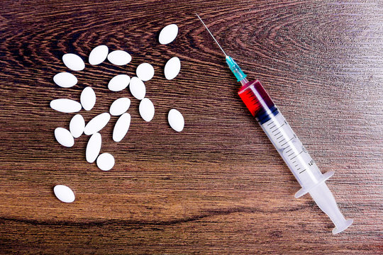 Pills and syringe isolated on wooden background