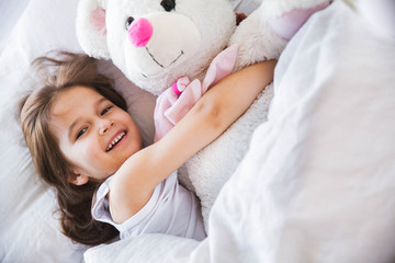 Obraz na płótnie Canvas beautiful little girl hugging her teddy bear in bed