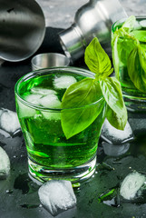 Cooling summer cocktail or liquor from basil leaves and ice. With shaker on black slate board on a gray stone table