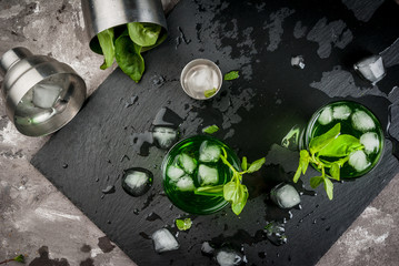 Cooling summer cocktail or liquor from basil leaves and ice. With shaker on black slate board on a gray stone table