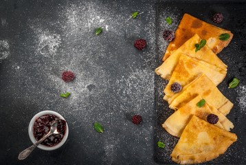 French crepes on a black slate board with fresh blackberries, mint leaves and jam, sprinkled with powdered sugar top view copy space