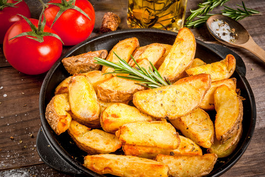 Fried potatoes in a rural style, with spices, rosemary and fresh tomatoes. On rustic pan, on a wooden table, close view copy space