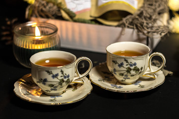 Two porcelain cups of tea on the black background with the candle