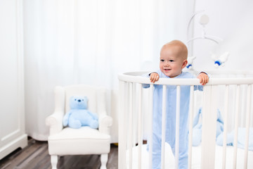 Baby boy standing in bed in white nursery