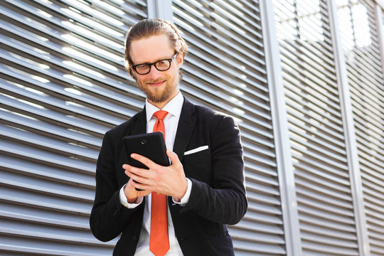 A businessman with a beard and glasses smiling and looking at tablet computer.