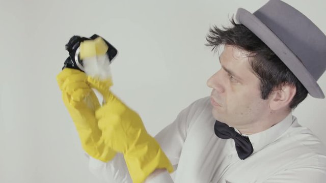 Man with Yellow Rubber Gloves Cleans a DSLR Photo Camera A funny guy with bow tie and hat brushing a digital DSLR Photo Camera. It looks a little like the mupped show. 