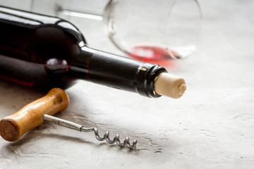 Bottle of red wine with corkscrew on white stone background