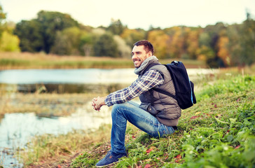 Naklejka na ściany i meble smiling man with backpack resting on river bank