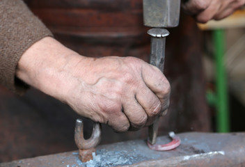 hand elder blacksmith who uses an iron awl and a hammer over a l