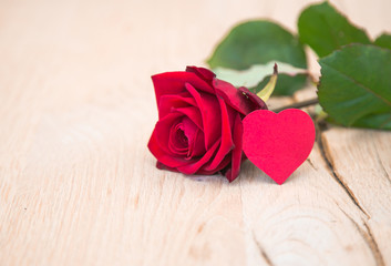 single red rose with heart shape paper on wood table
