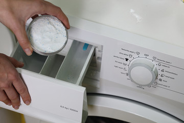 Close up on women hand puting laundry detergent into the washing machine