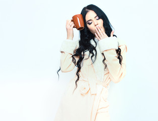 sexy yawning girl in beige velour bathrobe holding cup